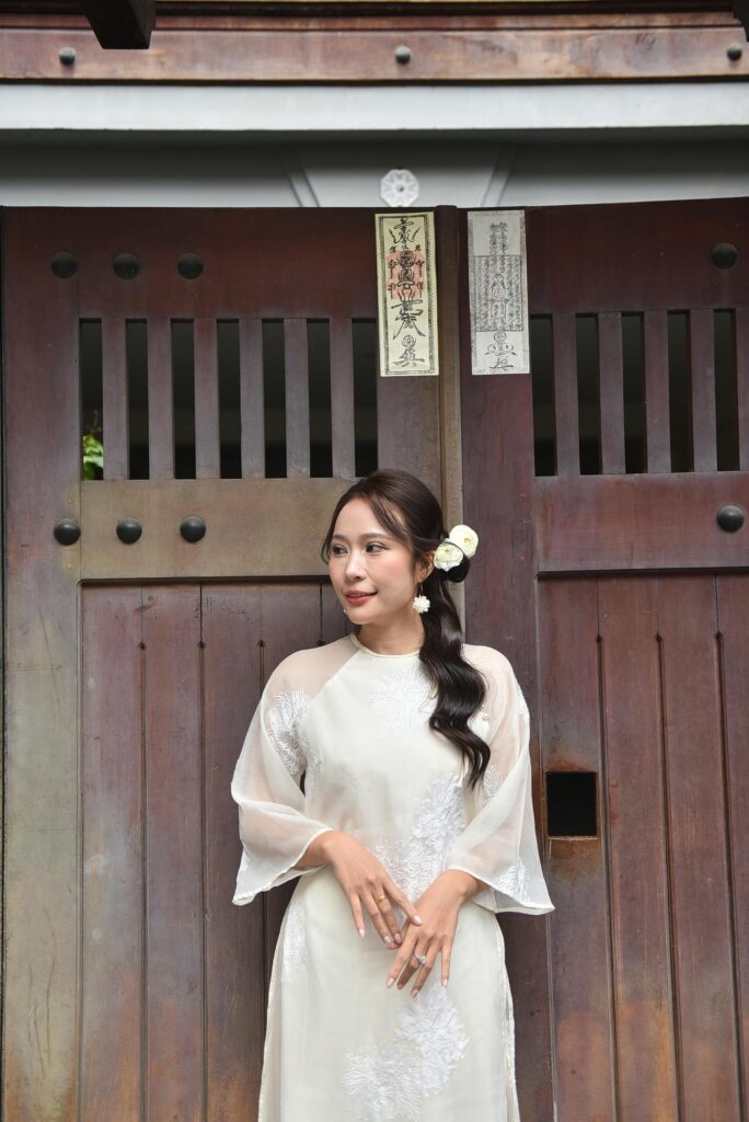 Woman in traditional attire posing in front of an Asian wooden gate, exuding cultural elegance.