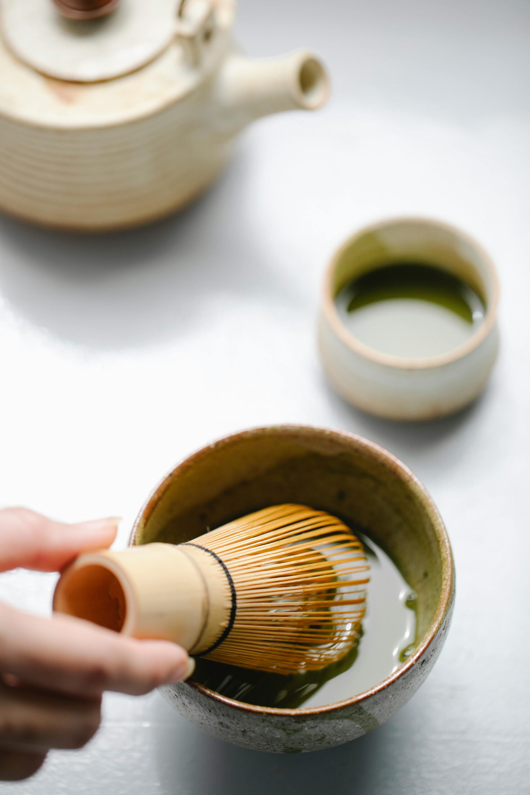 Close-up of hands preparing matcha tea with whisk and cup, indoors.